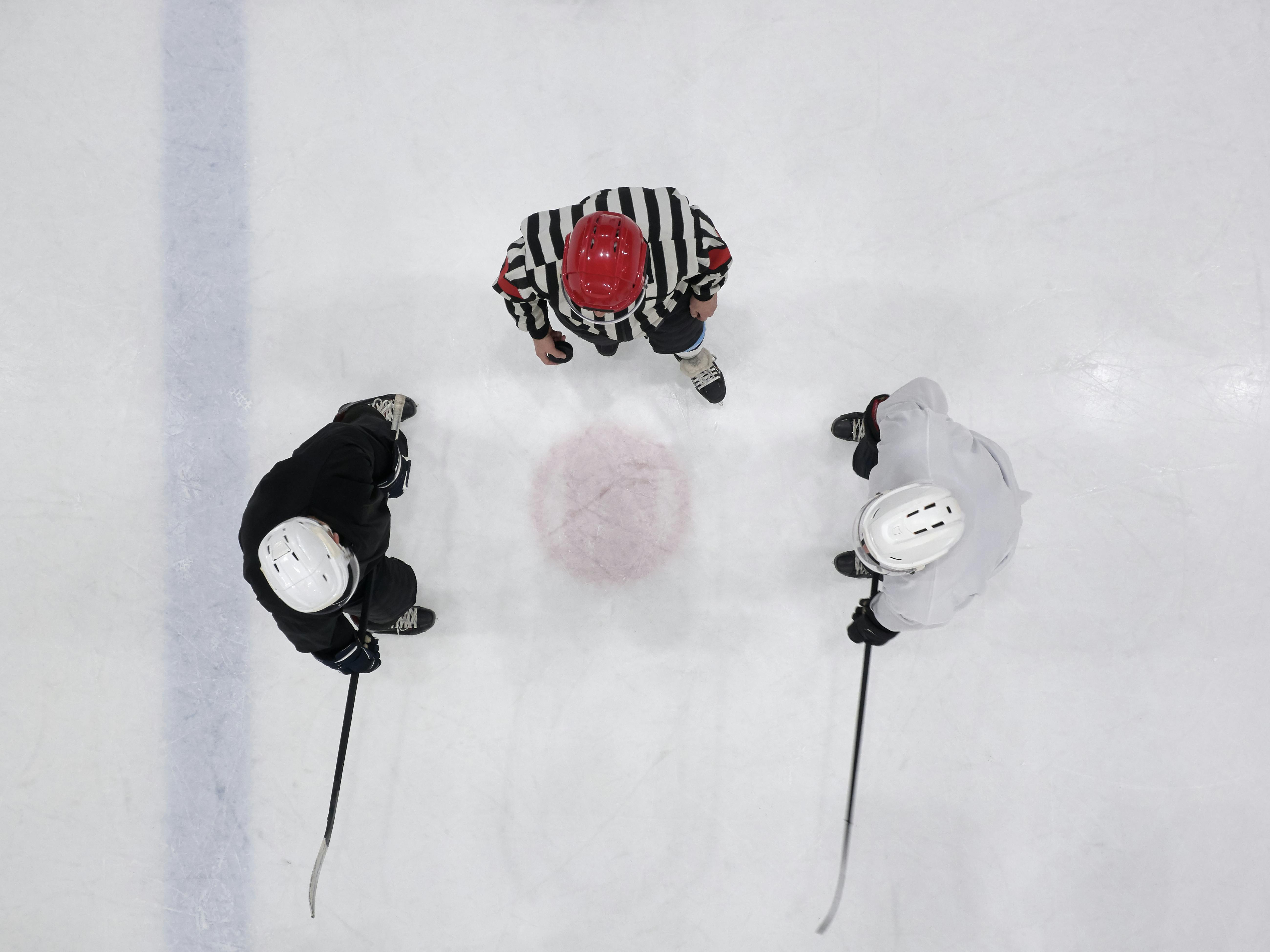 Overhead shot of ice hockey players and referee gathering on the rink for a faceoff.