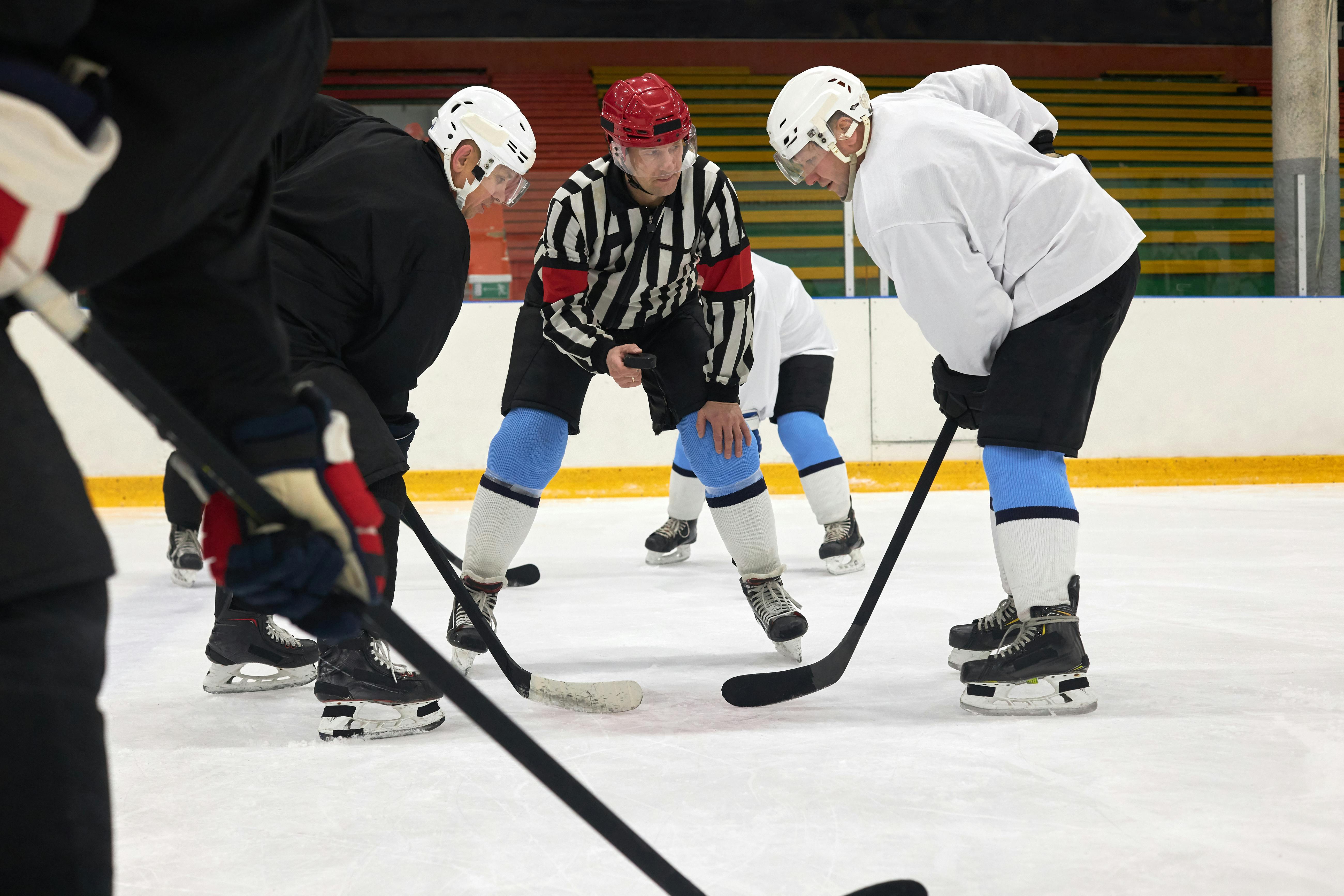 A referee drops the puck for a faceoff between players on an ice hockey rink.