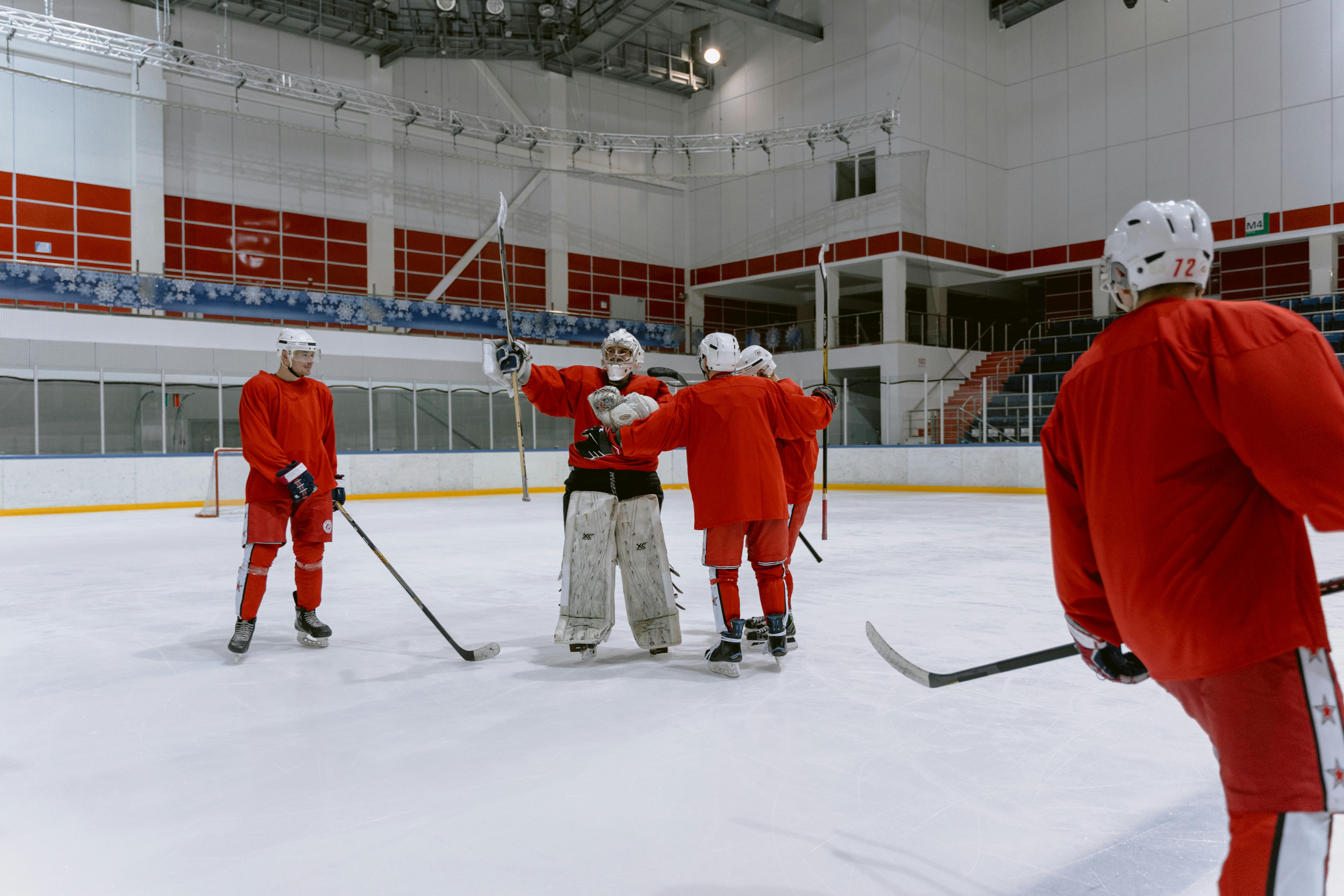 A group of ice hockey players in red jerseys celebrating on an indoor ice rink.