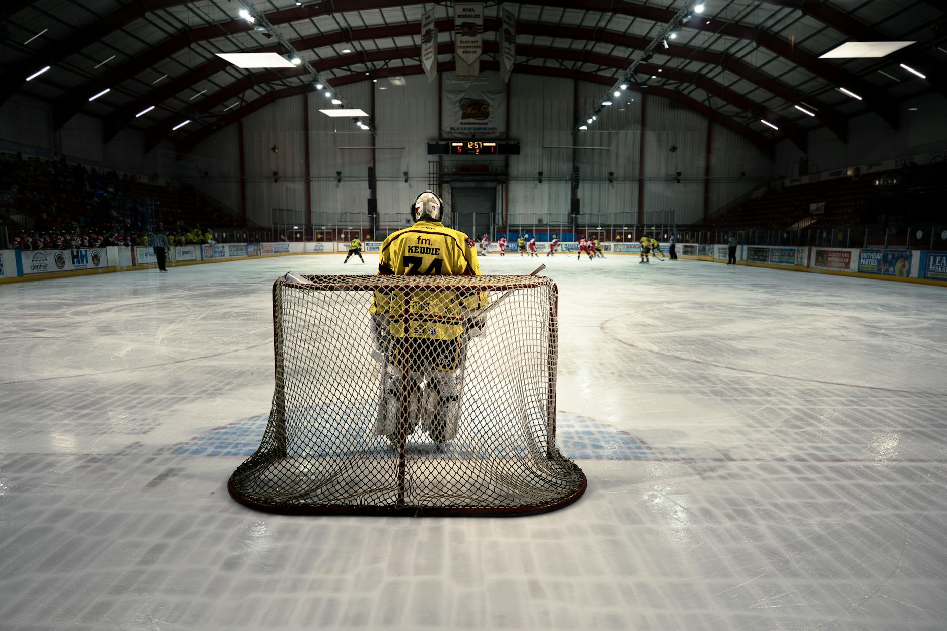 An ice hockey goalie stands in goal ready to defend during a competitive indoor match.
