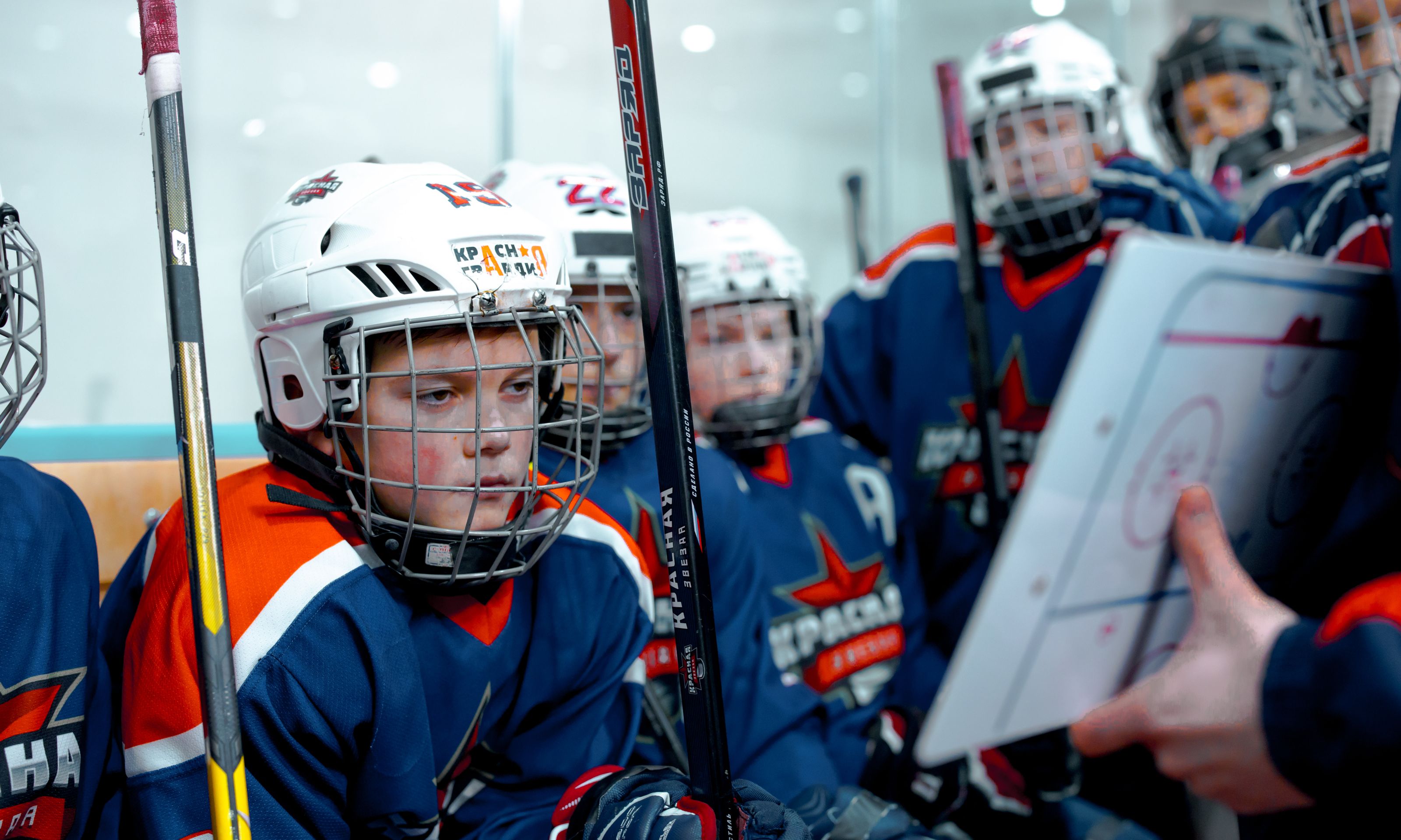 Young hockey players listen to coach's strategy during an ice hockey game in an indoor arena.